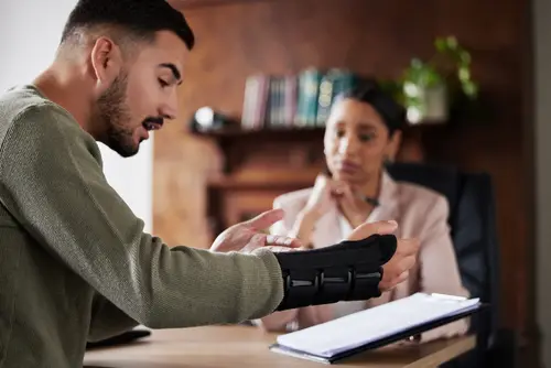 A man in an arm cast recieving help from a workers' compensation lawyer to help him during his workers' compensation claim process.