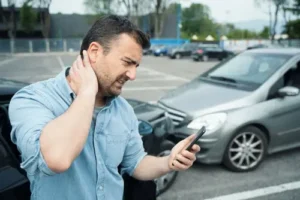 Injured man holding his neck and calling a Kennesaw car accident lawyer after a crash represented by Horst Shewmaker