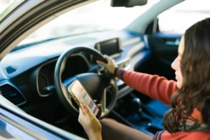 Woman sitting in her car using a smartphone representing a distracted driver that may hit a victim and cause the injured person to seek a distracted driving accident lawyer.
